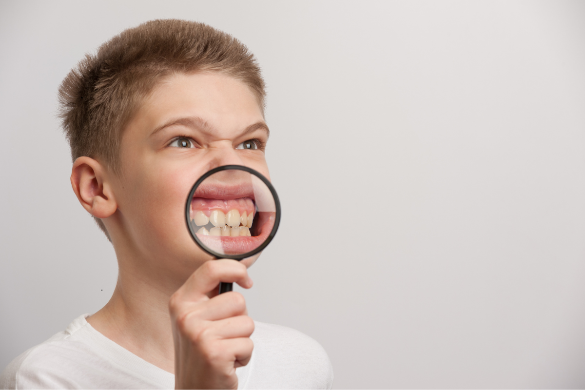 Boy holding magnifying glass revealing misaligned teeth, highlighting dietary impact on oral health.