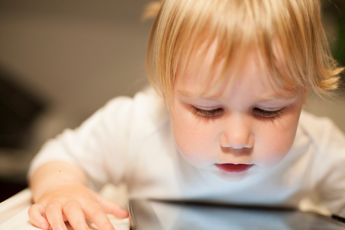 Toddler focused on tablet screen showing poor posture affecting jaw development.