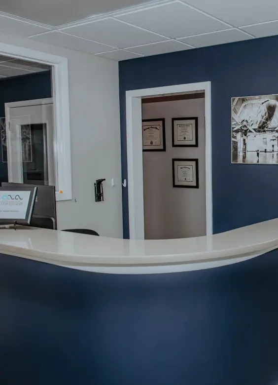 Modern dental practice reception desk with curved white counter and deep blue accent wall in Warren, Michigan.